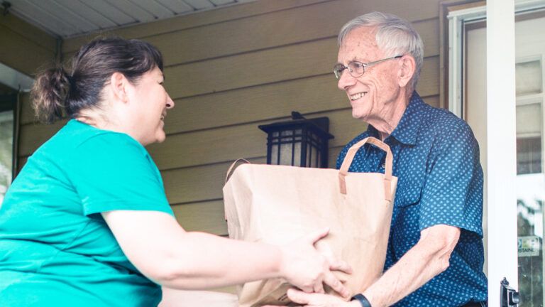 Royalty-free stock image: A woman brings her senior neighbor some groceries; Getty Images