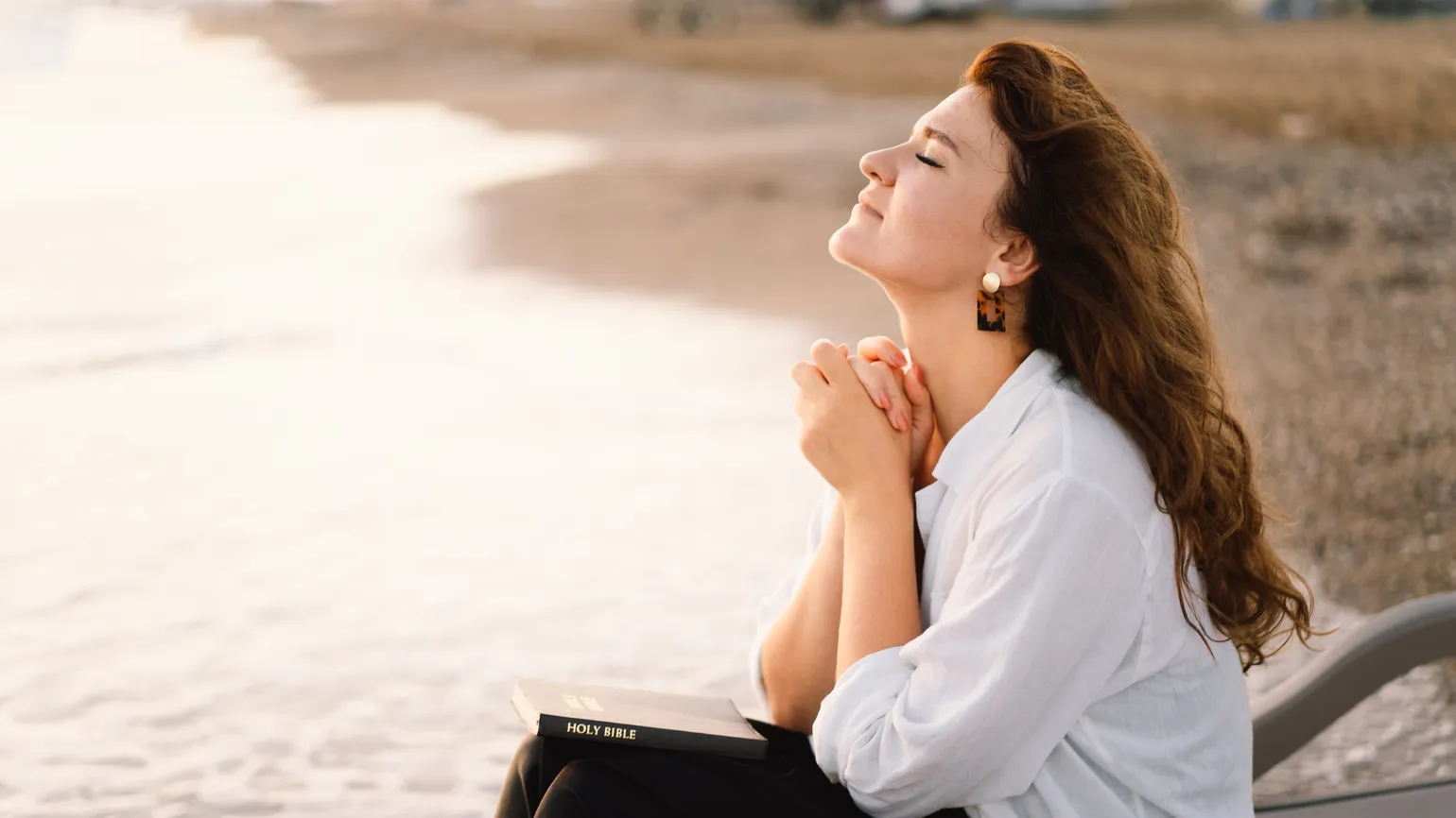 Woman on a beach with a bible in her lap doing her daily prayer habit