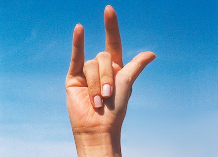 A photo of a hand signing 'I love you' against a blue sky