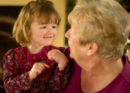 A young girl sits on her grandmother's knee listening to her sing.