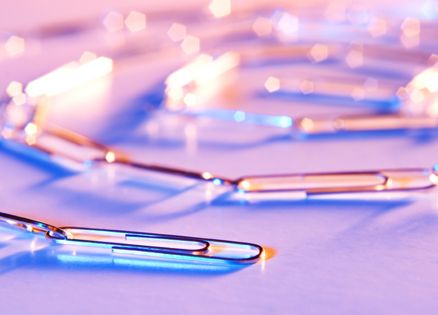 A chain of paper clips, colorfully lit and photographed on a table top