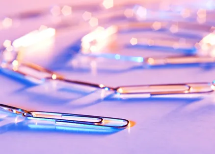 A chain of paper clips, colorfully lit and photographed on a table top