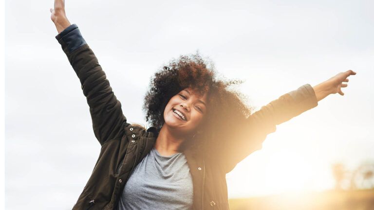 Woman with her arms in the air at sunset after reading devotions on gratitude