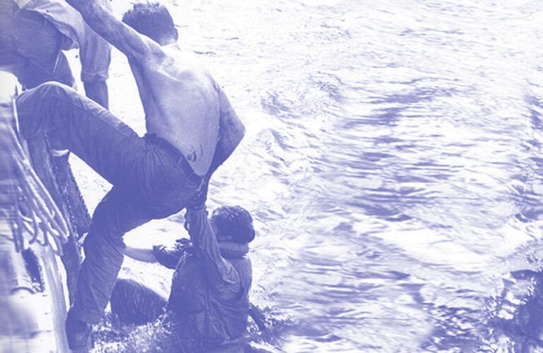 A sailor helps another sailor onboard from a lifeboat