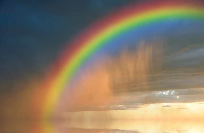 A bright and colorful rainbow bursting through a dark and cloudy sky