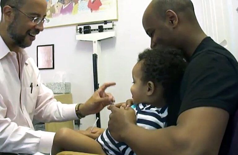 A doctor makes a toddler giggle even as he gives him a shot.