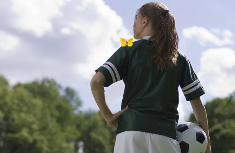 A young girl in a soccer uniform, with a yellow butterfly on her left shoulder