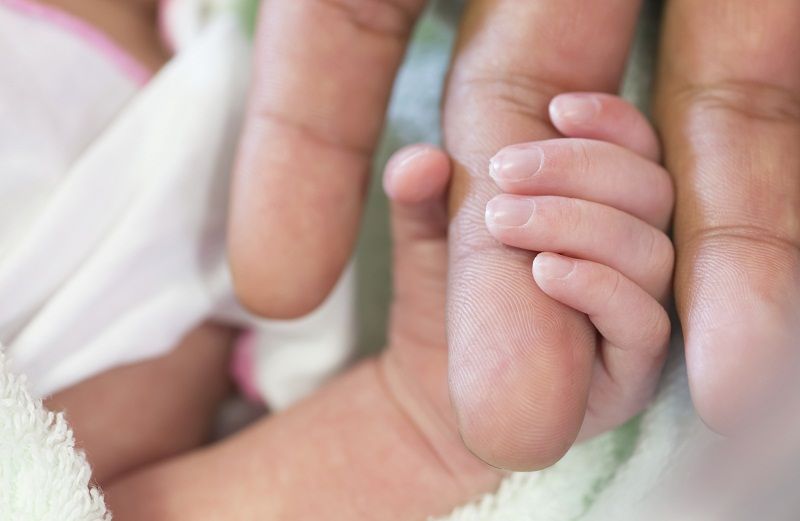 A newborn baby grabs the finger of his mom