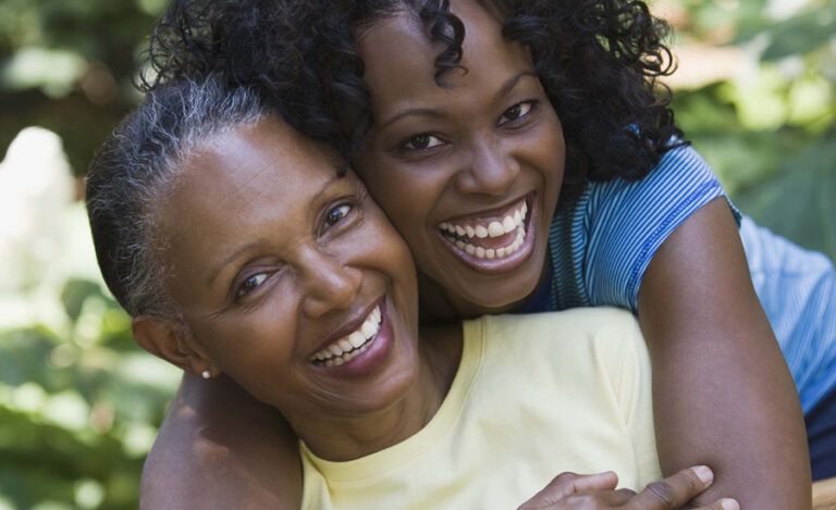 A mother and her adult daughter embrace with loving smiles