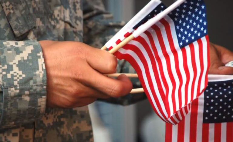 A veteran in combat fatiques holds a bundle of small American flags.