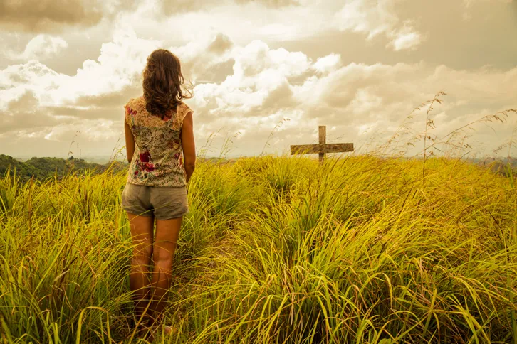 A woman in a field with a cross in front of her