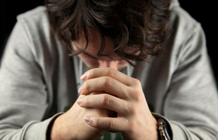 man's hands clasped in prayer as he prays The Lord's Prayer