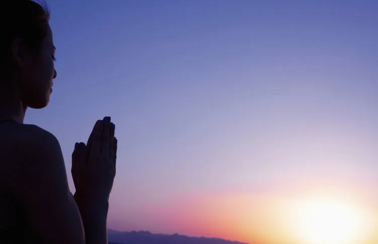 A woman in shadow prays as the sun rises