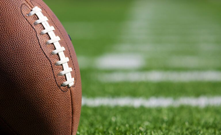 A football resting on green grass under a bright blue sky