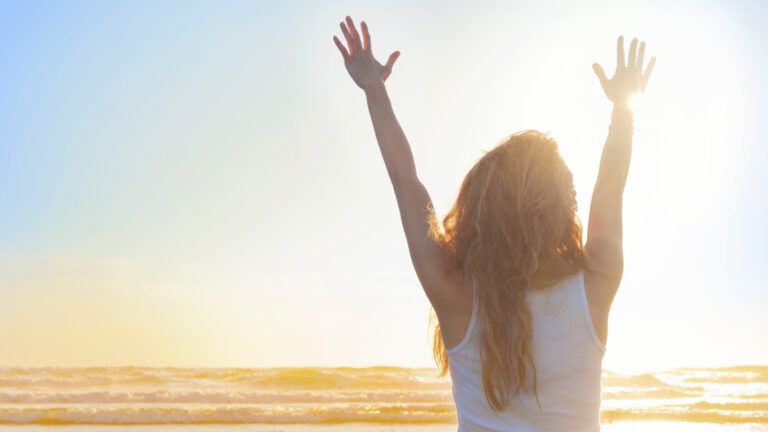 A woman with her hands up to the sun in victory.