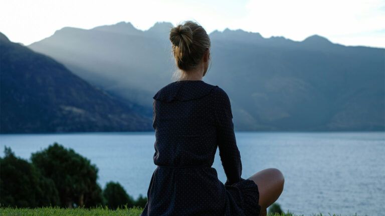 A woman sitting on grass looking out over a lake.