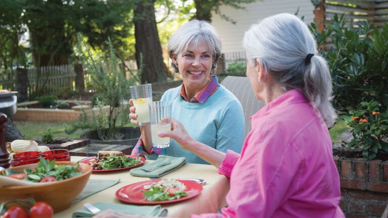 Two female friends enjoy a glass of lemonade together on a warm summer evening