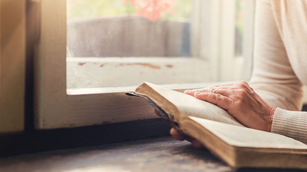 A woman reads her Bible by a window