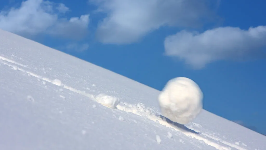 A large snowball tumbling down a snowy slope.