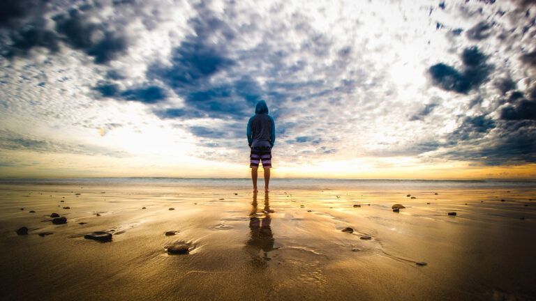 A young man stands on a beach at sunrise