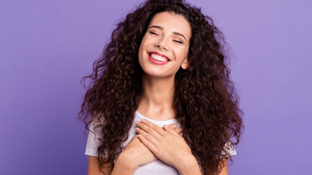 Woman on a purple background smiling for a lent prayer program with her hands on he heart