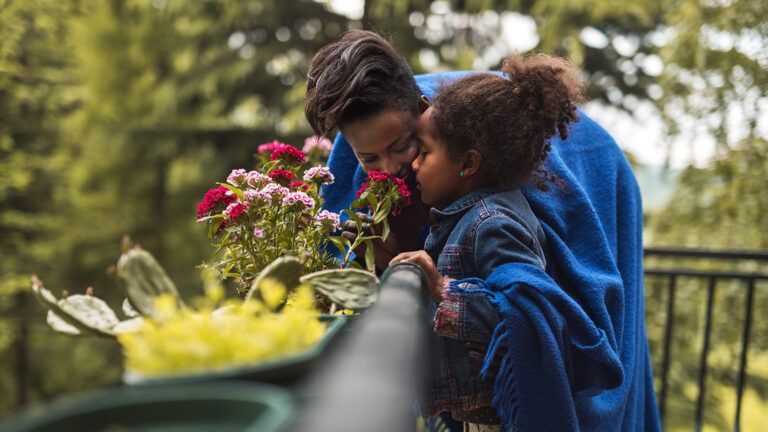 A mother and her young daughter stop to smell some flowers