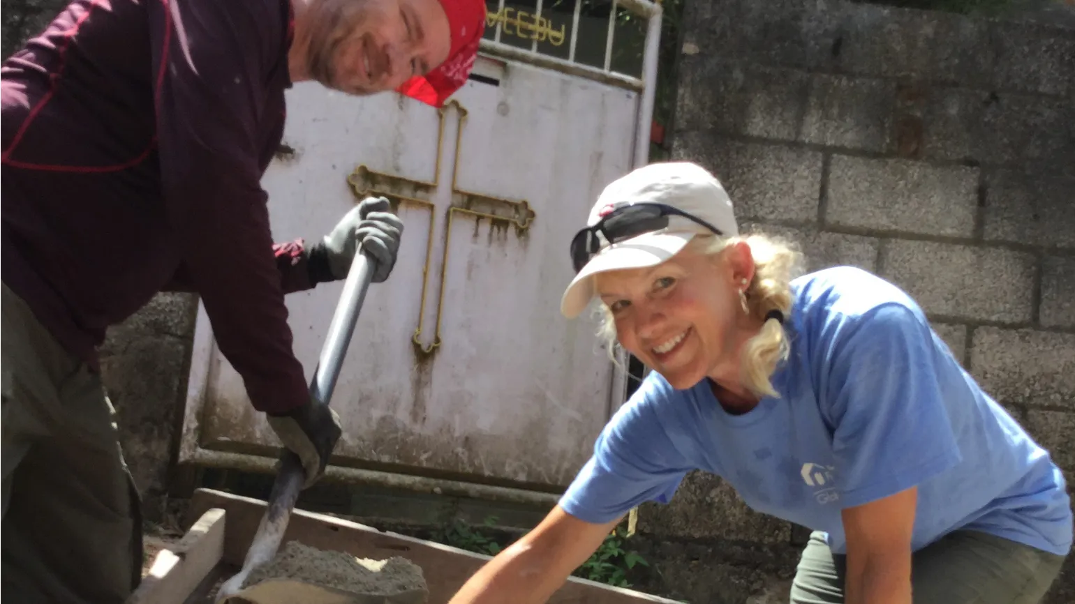 Two team members smile at the camera as they work on spreading concrete.