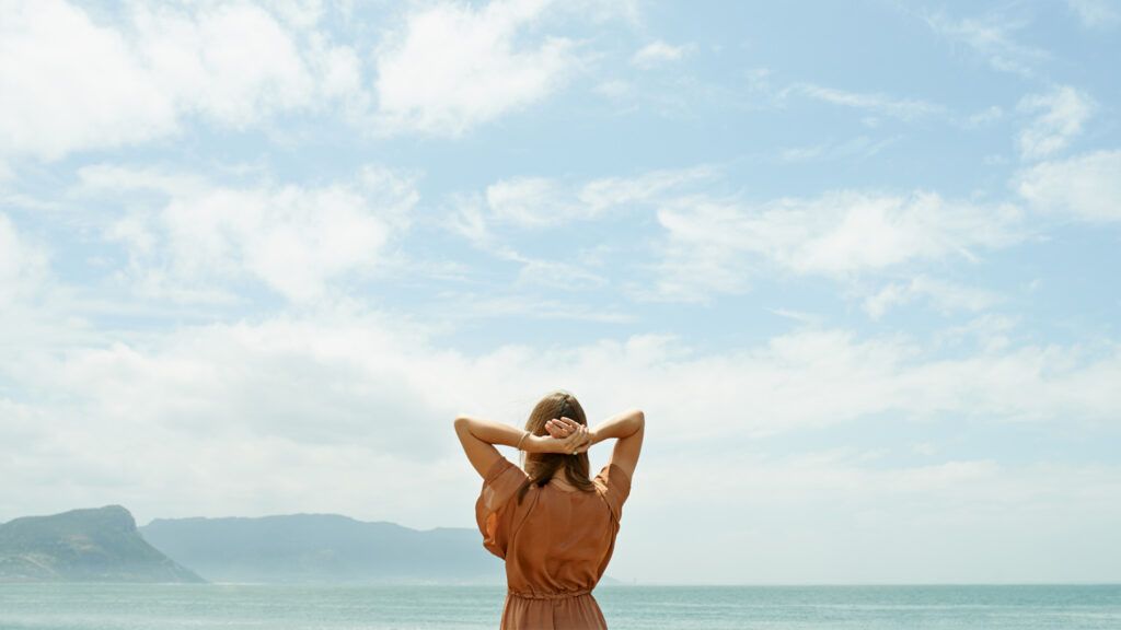 Rearview shot of a woman looking out at the ocean with sky above