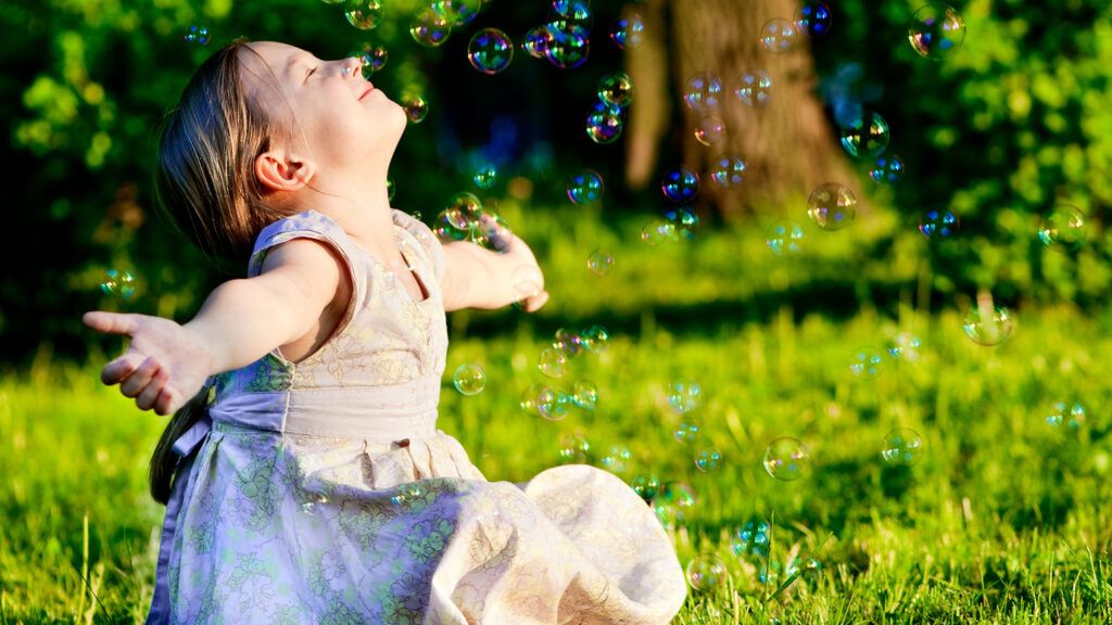 A young girl smiles as bubbles shes blown cascade down upon her.