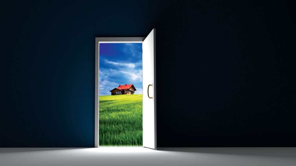 An open doorway in a darkened room looks out on a lovely home in the distance.