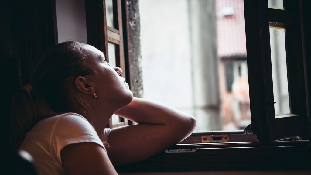 A woman looks heavenward out a window