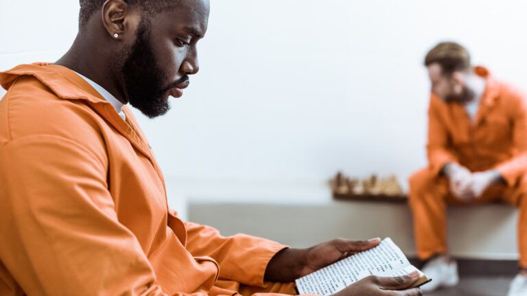 A convict reads a book in his jail cell.