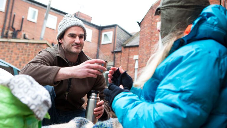 A man gives food to a homeless person