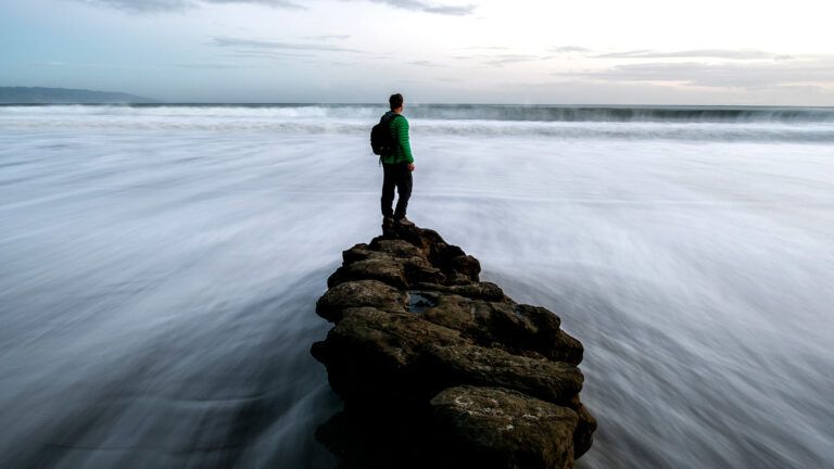 A man stands atop of pile of rocks as waters rush around him