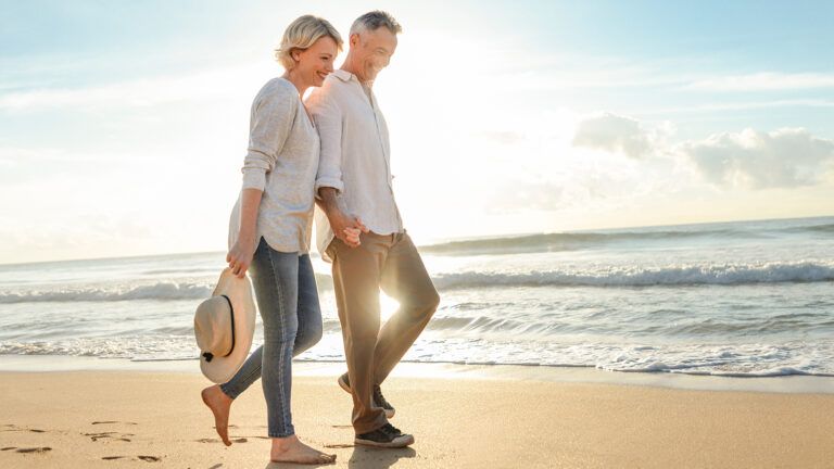 A Mature Couple stroll hand-in-hand along a beach