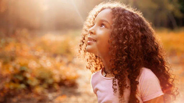 A little girl looking up into the sunlight on a warm, Autumn day.