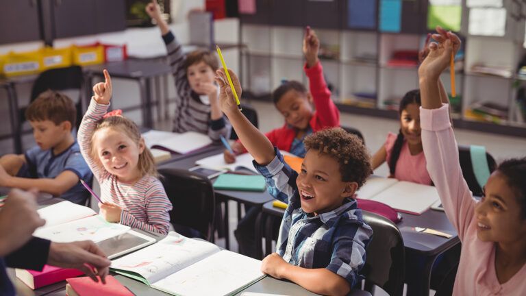 Smiling children raise their hands in a classroom