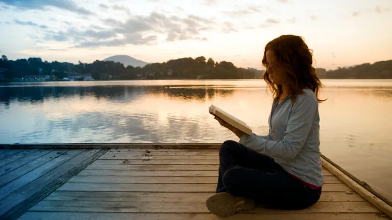 A woman peacefully reading a book by the pier.