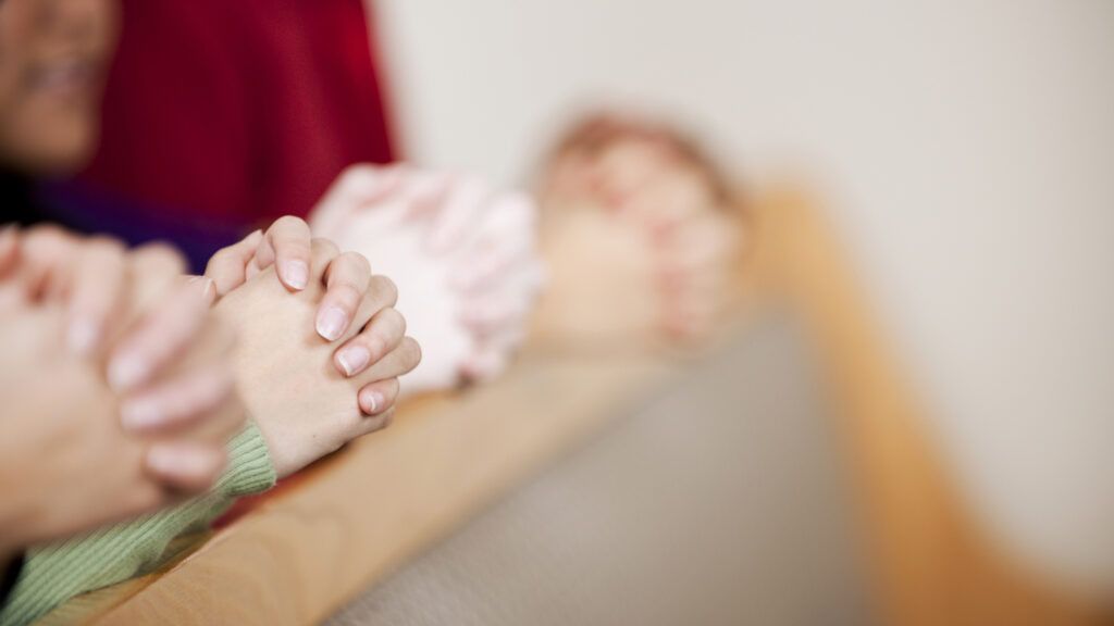 Hands in prayer in the pews of a church.