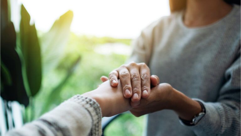 Women holding each other hands for comfort and sympathy.