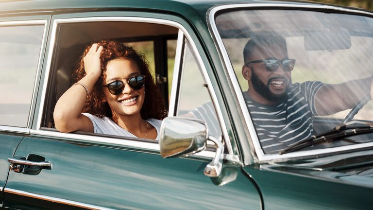 A smililng woman smiles from her car on a road trip