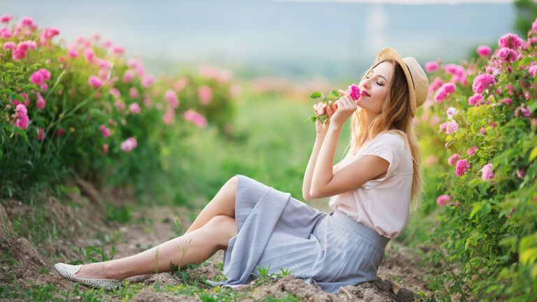 A woman  smells a flower while sitting in a sunny field