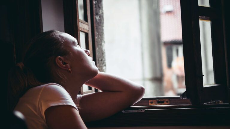 A woman gazes upward through a window