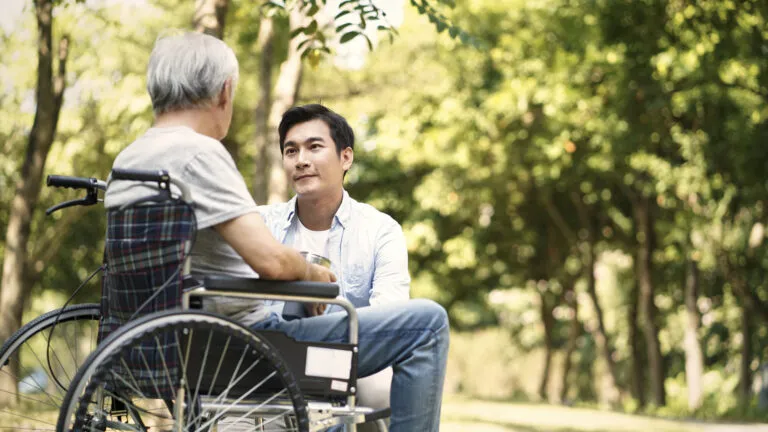 An aging mother in wheelchair converses with her caregiver son.