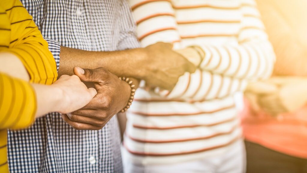 A multicultural group of people clasp hands in unity