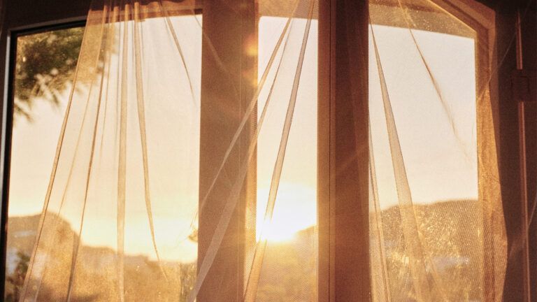 Sun is shining through sheer curtains of a window. Credit: Unsplash