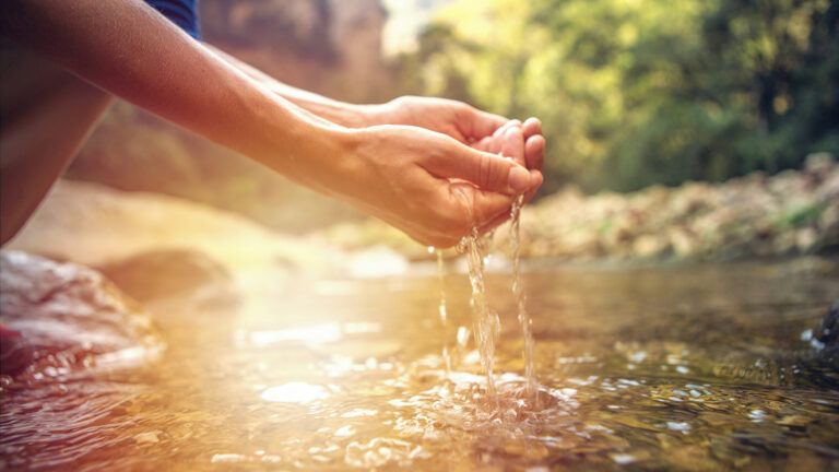 A woman dips her hands into spring water