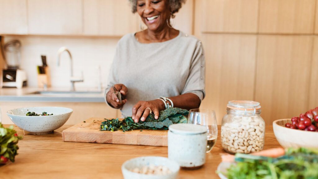 A woman cutting vegeatbles in her kitchen; Getty Images