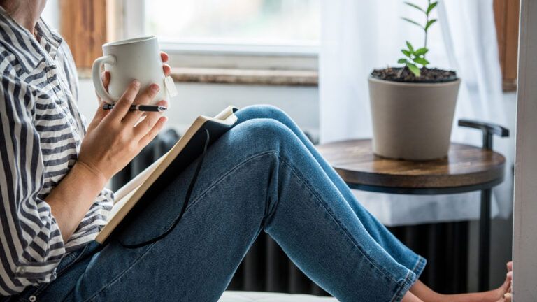 A woman journaling beside a window; Getty Images