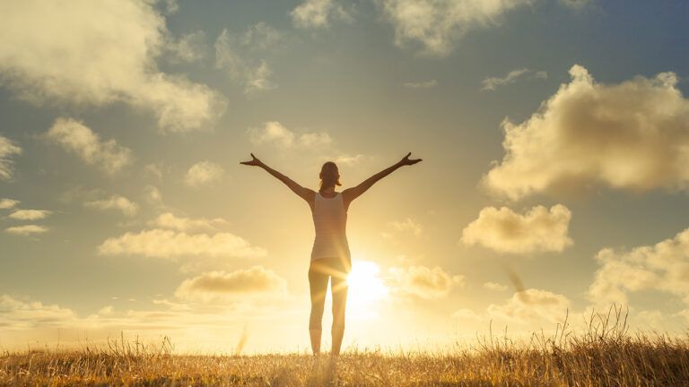 A woman greets the sunrise, arms upraised